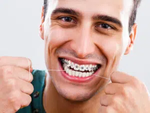 Man flossing teeth with braces as part of a daily braces care routine
