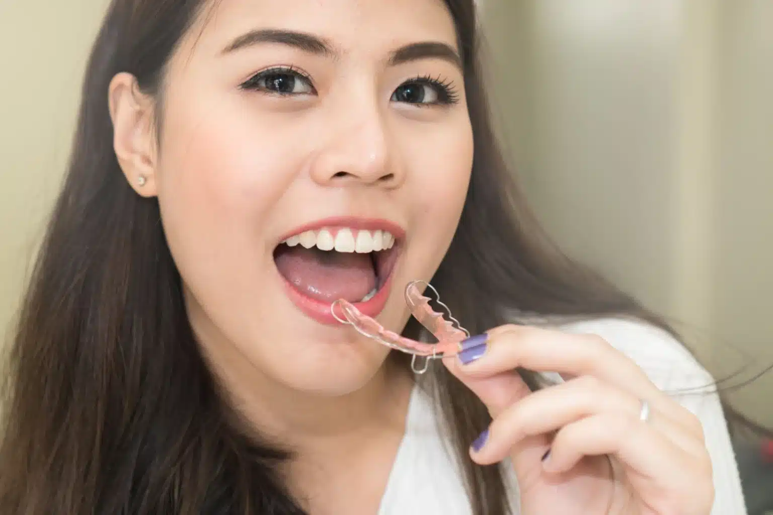 Asian woman smiling while wearing a clear teeth retainer